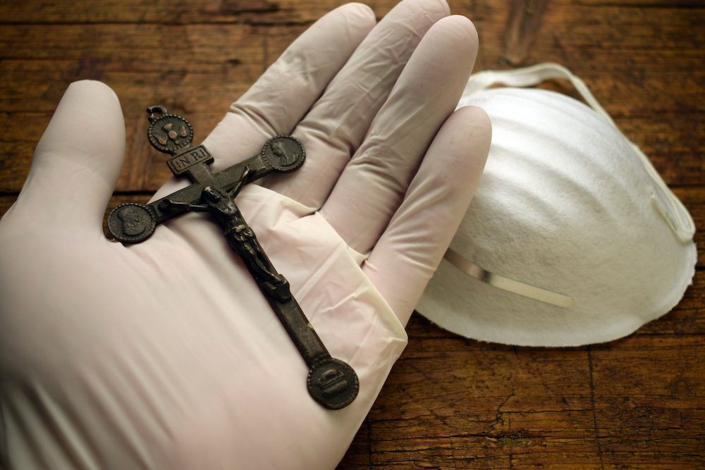 gloved hand holding crucifix above mask